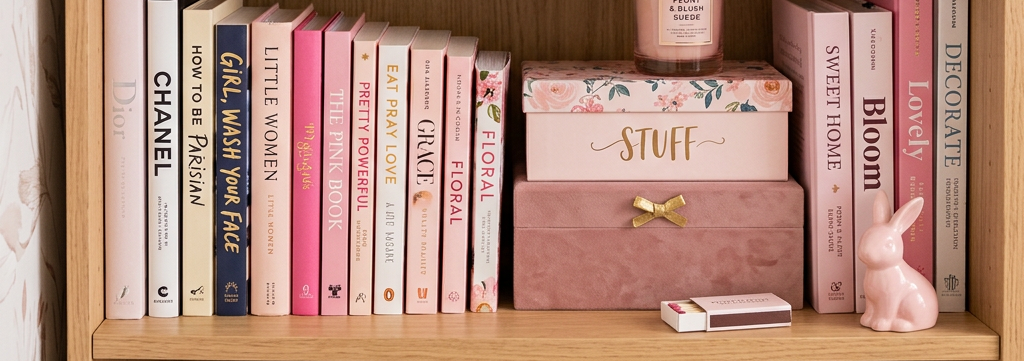 Bookshelf with pink books, decorative boxes labeled 'STUFF', small Eiffel Tower figurine, potted succulent, candle, and inspirational framed quotes